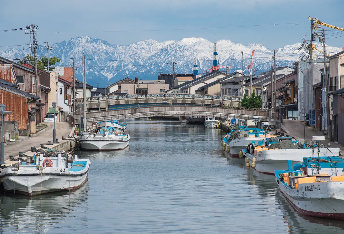 雪をいただいた立山連峰を背景に、富山県射水市内川に浮かぶ漁船群と東橋